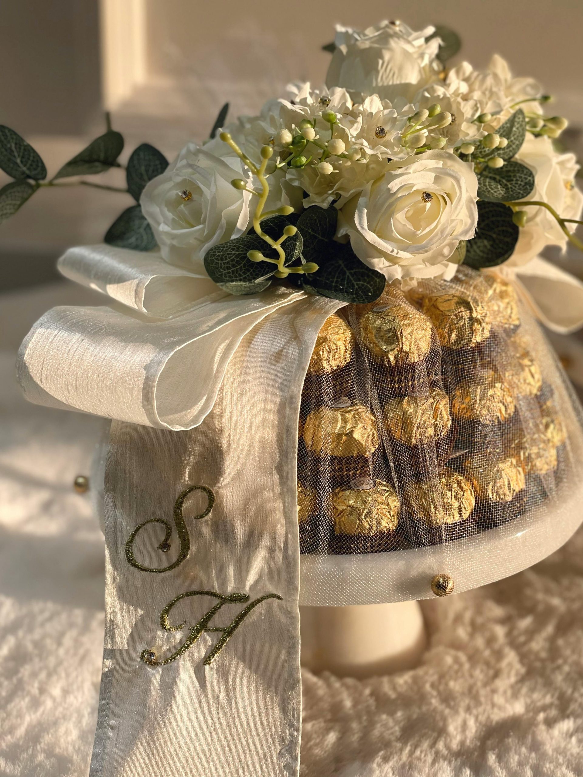 Luxurious Ferrero Rocher tower adorned with white roses and ribbon.